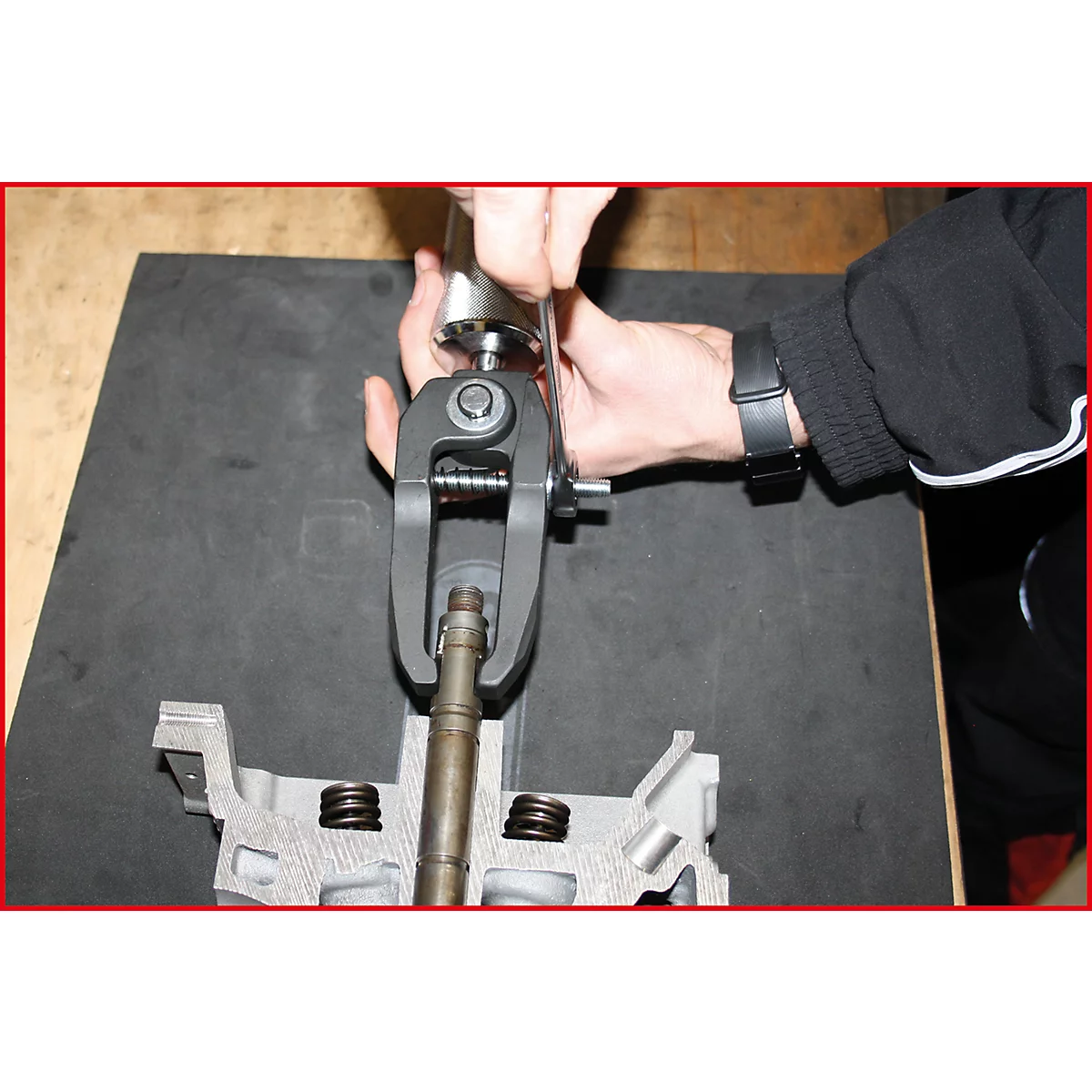 Person hantiert Werkzeug an einem Motorteil. Ein schwarzes Werkzeug wird eingesetzt, um eine Feder zusammenzudrücken.